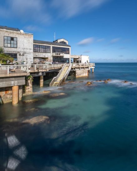 Exterior of the Aquarium building over the water on a clear blue day, ocean visible beneath the deck