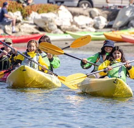 Students smiling while sitting in yellow kayaks on the water