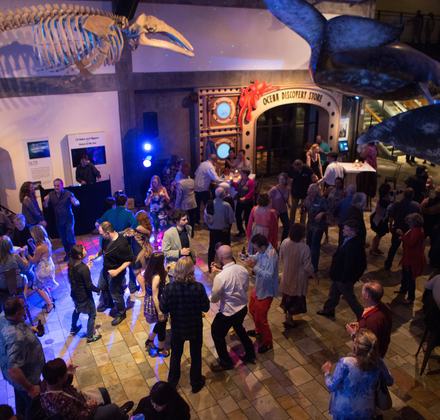 Guests dancing at an evening member event inside Monterey Bay Aquarium's main hall