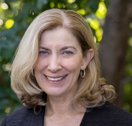 Headshot of Dr. Jenny Gray smiling outdoors with soft green foliage in the background