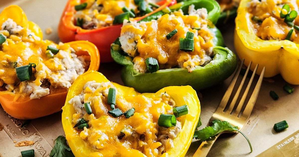 Stuff bell peppers halves filled with canned albacore tuna and rice mixture, topped with melted cheddar cheese, chopped green onions, and herbs, on a plate with one fork